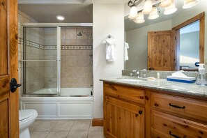 Een badkamer met douche, toilet, bad, houten kastjes en een wastafel.