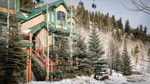 A multi-story building with a green roof and wooden staircase, surrounded by snow-covered ground and evergreen trees.