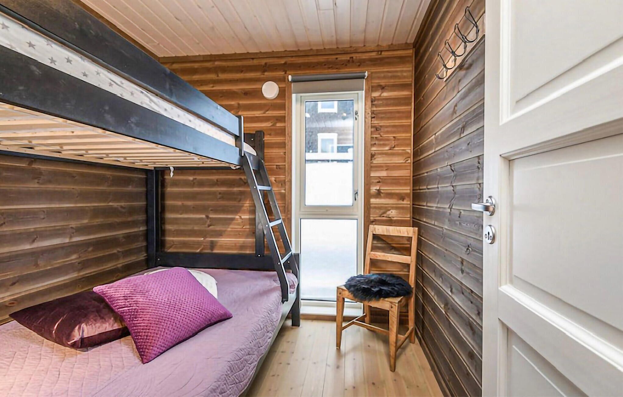 Ein kleines, blockhausartiges Zimmer mit einem Etagenbett, einem kleinen Holzstuhl und einer Tür zu einem Außenbereich.