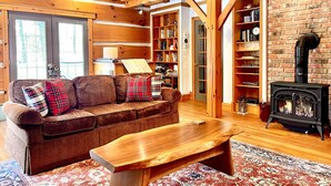 A cozy living room with a wooden ceiling, a fireplace, a sofa with plaid cushions, and a bookshelf. - Luxury Log Home, Southern Georgian Bay - Explore Blue Mountain to Tobermory (Annan)