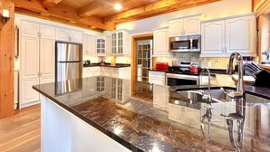 A spacious kitchen with white cabinetry, a large granite island, stainless steel appliances, and a wooden ceiling. - Luxury Log Home, Southern Georgian Bay - Explore Blue Mountain to Tobermory (Annan)