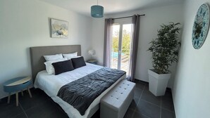 A modern bedroom with a bed, bench, bedside table, potted plant, and a view of the outside. - Villa Coquelicot - Private swimming pool - Electricity terminal (Moussac)