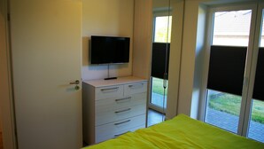 Un dormitorio con cama, cómoda, televisor y puerta corrediza de vidrio que da a un espacio exterior.