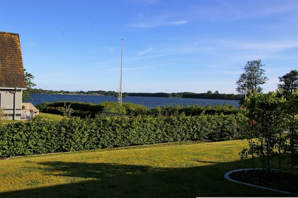 A grassy area with a body of water, a flagpole, and a building with a sloped roof.