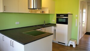 Una cocina compacta con armarios blancos, una campana extractora de acero inoxidable, un horno empotrado y un taburete blanco pequeño.