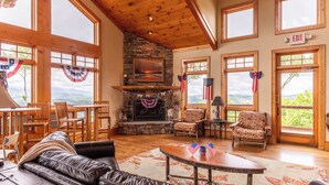 A spacious living area with a stone fireplace, wooden furniture, and large windows offering scenic views.