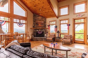 A spacious living area with a stone fireplace, wooden furniture, large windows, and a view of the outdoors.