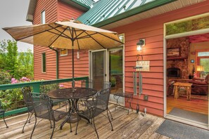 A wooden deck with a table and chairs, a large umbrella, and a sign reading "ONE SIT ON THE PINCH WITH ME".