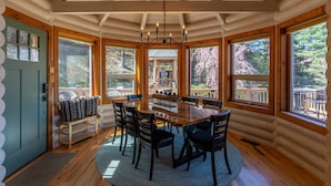 Eine Holzhütte mit Essbereich, ausgestattet mit einem Holztisch und Stühlen, großen Fenstern und Blick auf den umliegenden Wald.