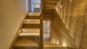 Un escalier en bois, doté d’une rampe, mène à une pièce aux murs en bois et au plafond orné de poutres en bois.