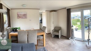 Una sala de estar moderna con comedor, sofá, televisor y puerta corrediza de vidrio que da a un jardín.