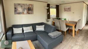 Una sala de estar moderna con un sofá seccional gris, una mesa de centro de madera y un comedor con una mesa de madera y sillas grises.