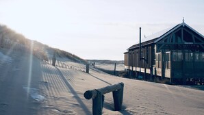 Un edificio de madera con un letrero que dice "DE ZWALUW" cerca de una playa arenosa con una valla de madera.