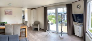 Een moderne woonkamer met een eethoek, een bank, een televisie en een schuifdeur die uitkomt op een tuin.