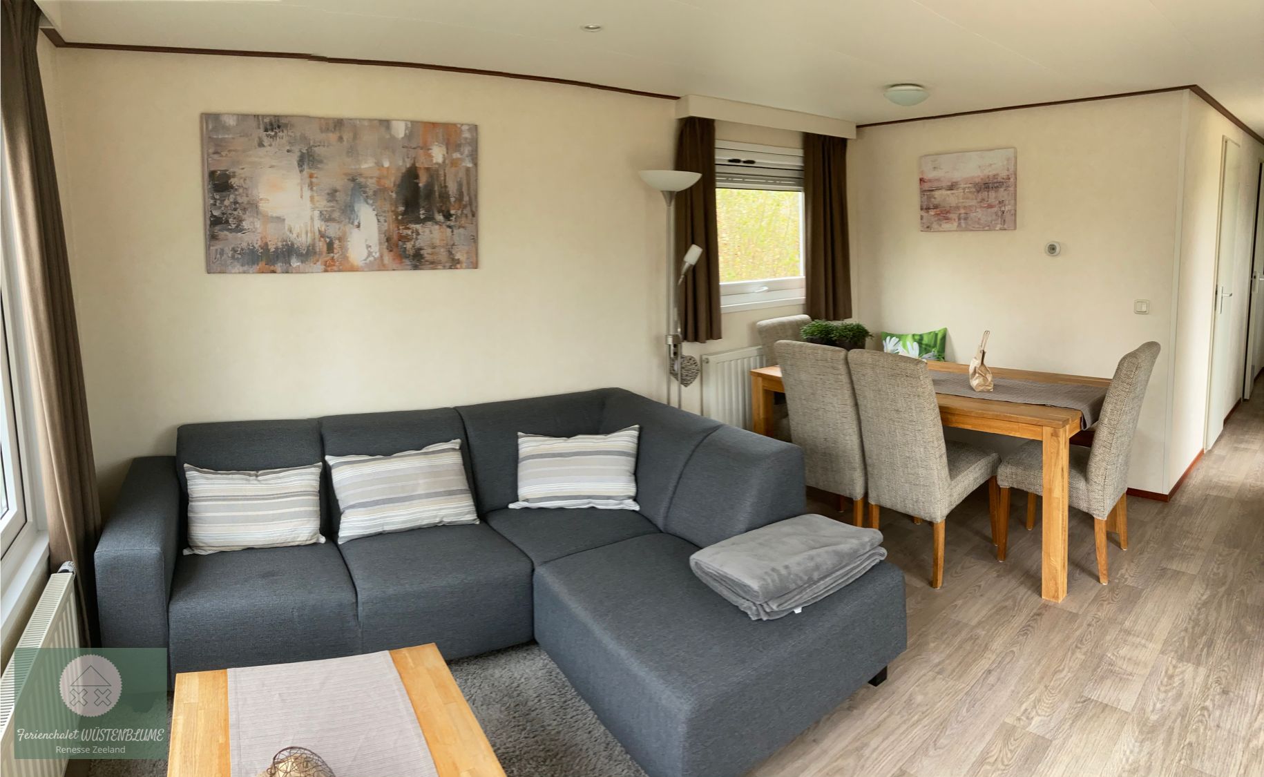 A modern living room with a grey sectional sofa, a wooden coffee table, and a dining area with a wooden table and grey chairs.