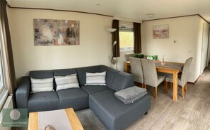 Een moderne woonkamer met een grijze modulaire bank, een houten salontafel en een eethoek met een houten tafel en grijze stoelen.