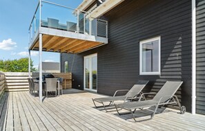 Una casa moderna con terraza, balcón de cristal y dos sillones de descanso.