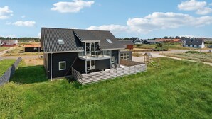 A modern two-story house with a balcony, surrounded by a grassy area and other houses in the background. - Lovely home in Thisted (Thisted)