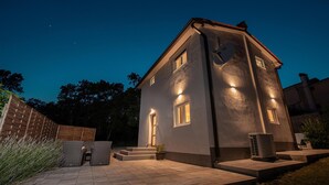 Et moderne hus med skråt tag, en parabolantenne og et lille udendørs siddeområde med stole og et bord.