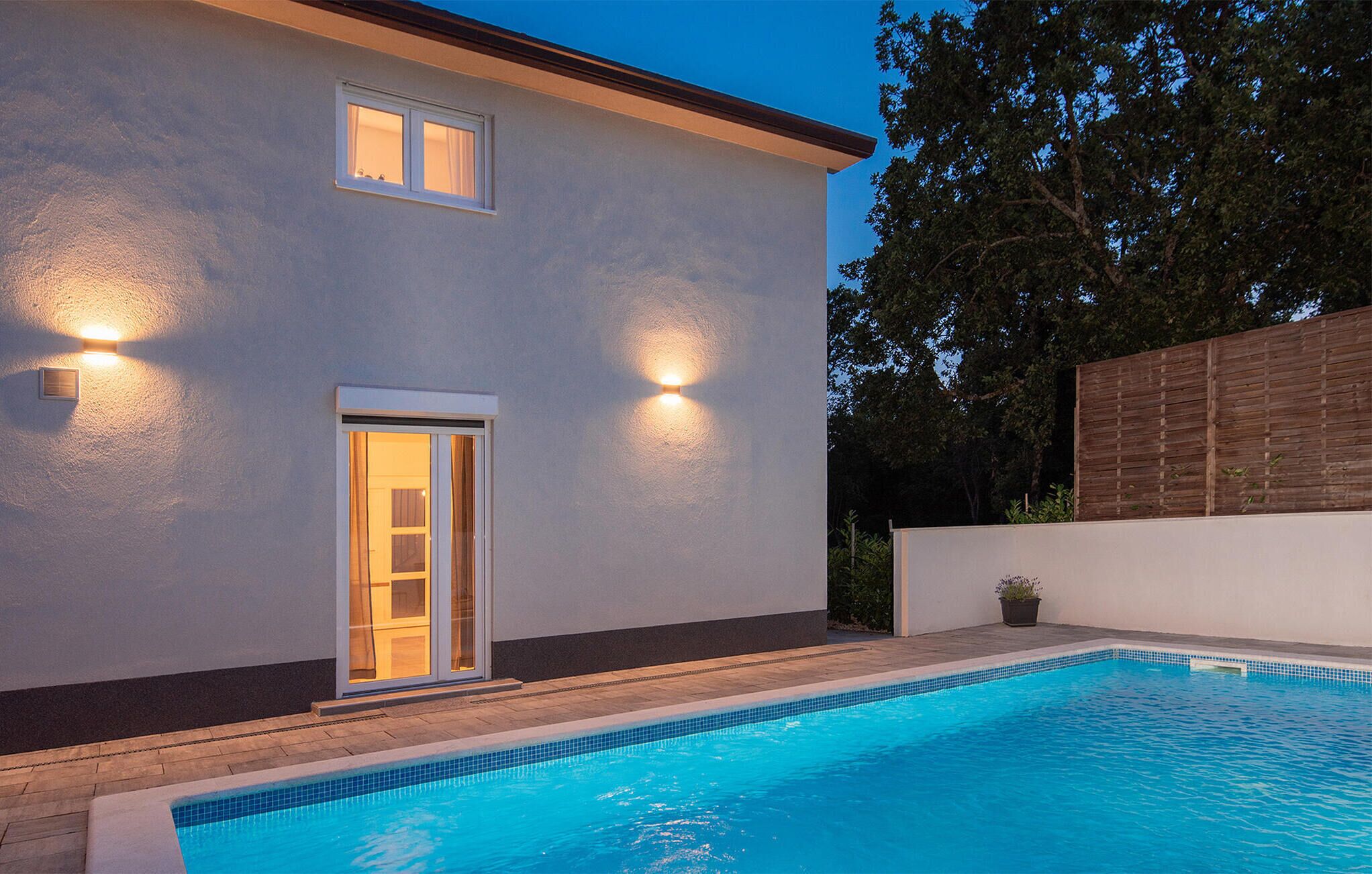 Een modern huis met een zwembad, een deur met glaspanelen en twee buitenverlichtingen.