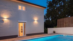 Et moderne hus med swimmingpool, en dør med glaspaneler og to udendørs væglamper.