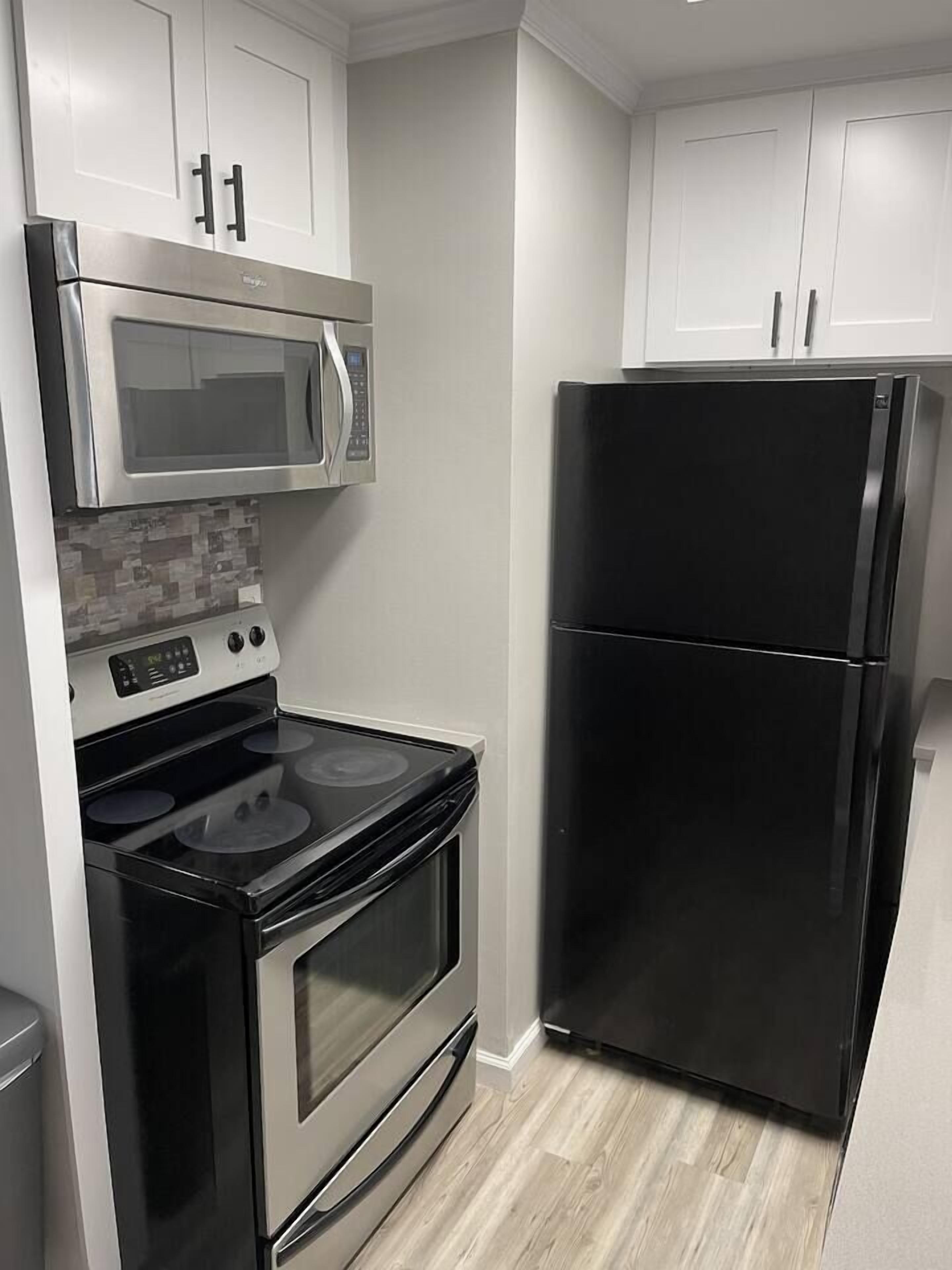 Una cocina compacta con microondas, horno y refrigerador de acero inoxidable, todo en color negro.
