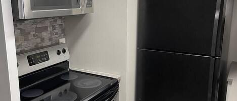 Una cocina compacta con microondas, horno y refrigerador de acero inoxidable, todo en color negro.