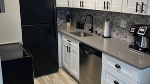Una cocina moderna con gabinetes blancos, un refrigerador negro, lavavajillas de acero inoxidable y una cafetera.