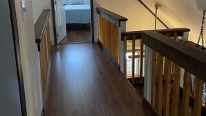 A narrow, wooden-floored hallway with a sloped ceiling leading to a bedroom.