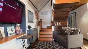 A living room with a TV, a sofa, a patterned rug, a staircase, and a ceiling fan.