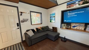 A modern living room with a sectional sofa, a mounted TV, a wooden floor, and a door with a handle.