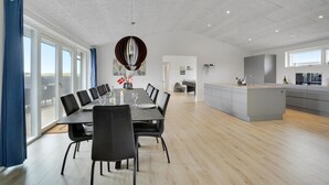 Et moderne spiseområde med et langt bord, sorte stole og en unik pendellampe.