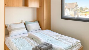 Quarto com cama, almofadas, cobertor, janela e guarda-roupa de madeira.