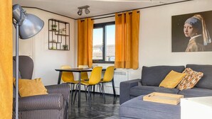 Uma sala de estar moderna com um sofá cinza, cadeiras amarelas, um sofá listrado em preto e branco, uma escrivaninha com abajur e uma janela com cortinas laranja.