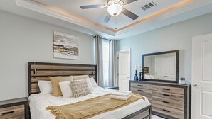 Une chambre à coucher avec un grand lit, une tête de lit en bois, des tables de chevet, une commode, un ventilateur de plafond et un grand miroir.