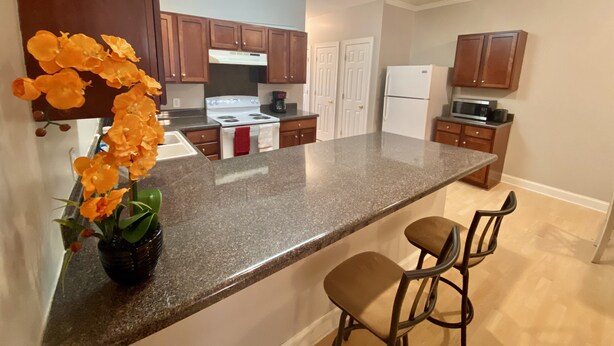 A modern kitchen with granite countertops, wooden cabinets, a white refrigerator, and a built-in oven.