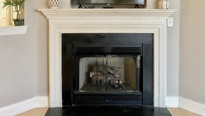 A living room with a fireplace, a flat-screen TV mounted above it, and a small vase with flowers on the mantel.