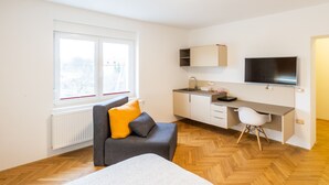 A modern room with a bed, a grey sofa with yellow cushions, a desk with a chair, a TV, and a window with blinds. - Apartments Kamr'ca - room 2 & 5 with private bathroom (Ljubljana)