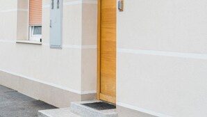 A building facade with a wooden door, a window with blinds, and a small step leading to the entrance. - Apartments Kamr'ca - room 2 & 5 with private bathroom (Ljubljana)