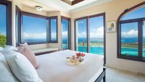 A bedroom with a large bed, a tray with breakfast items, and a view of the ocean through large windows.