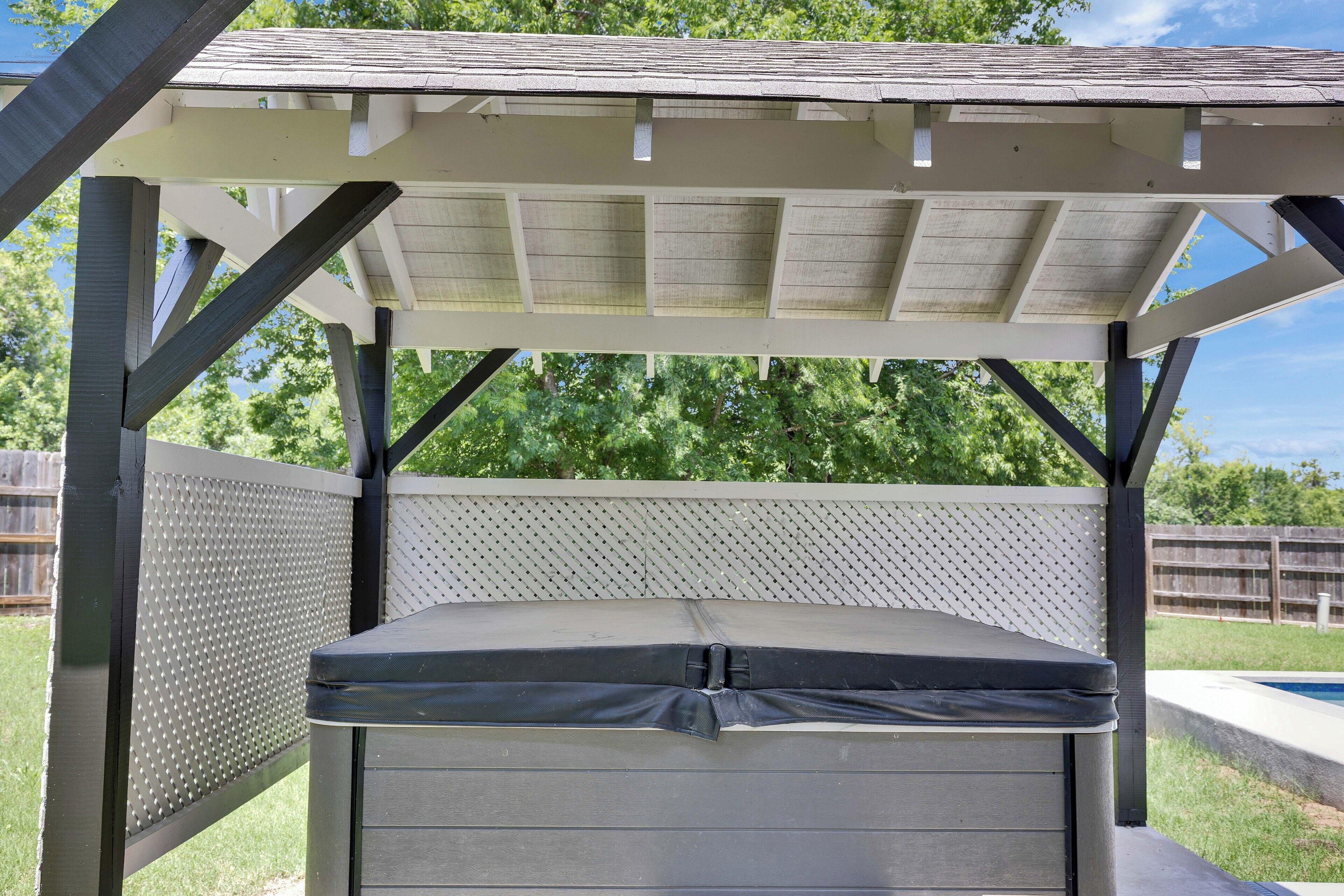 Un espace extérieur abrité, avec un banc et une table, entouré d’une clôture et d’arbres.