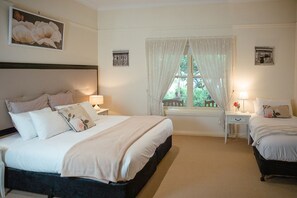 A bedroom with a large bed, two bedside tables, a window with curtains, and a small table with a lamp.