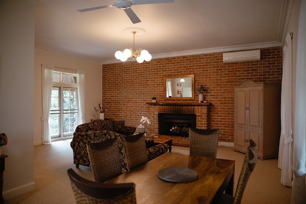 A living room with a brick fireplace, a ceiling fan, and a dining area with a wooden table and chairs.