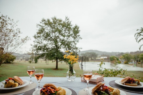 A table set with food and drinks, overlooking a lake and trees.