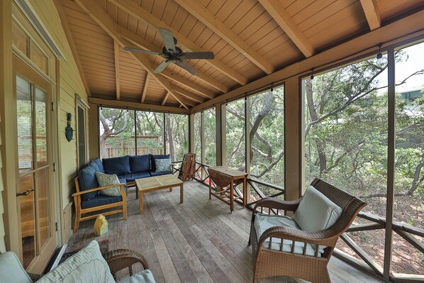A covered porch with wooden flooring, a ceiling fan, and a seating area with a sofa and chairs. - Bikes & beach gear in shed! Quick walk to community pool & beach access. (Seacrest)