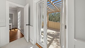 Corredor com piso de madeira que leva a uma porta com vista para uma pérgola de madeira e área de estar ao ar livre.