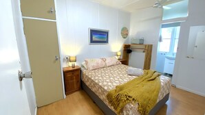 A bedroom with a bed, bedside lamps, a nightstand, a wooden shelf, and a window with a view. - Exmouth Villas Unit 28 - This Villa is Perfect for groups and families alike (EXMOUTH)