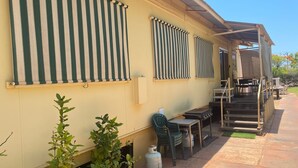 A yellow building with green-striped awnings, outdoor seating, and a gas cylinder. - Exmouth Villas Unit 28 - This Villa is Perfect for groups and families alike (EXMOUTH)
