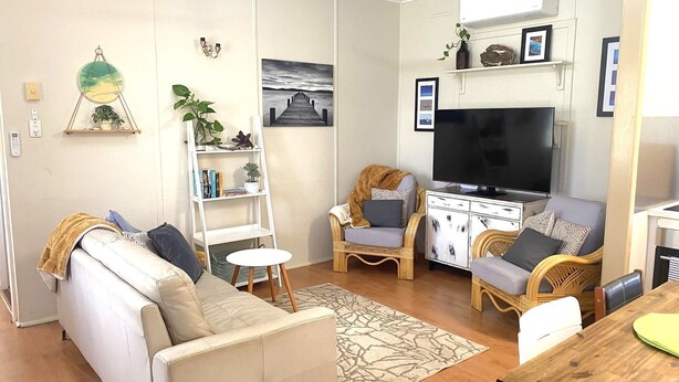 A living room with a sofa, two armchairs, a TV, a bookshelf, and a painting on the wall. - Exmouth Villas Unit 28 - This Villa is Perfect for groups and families alike (EXMOUTH)