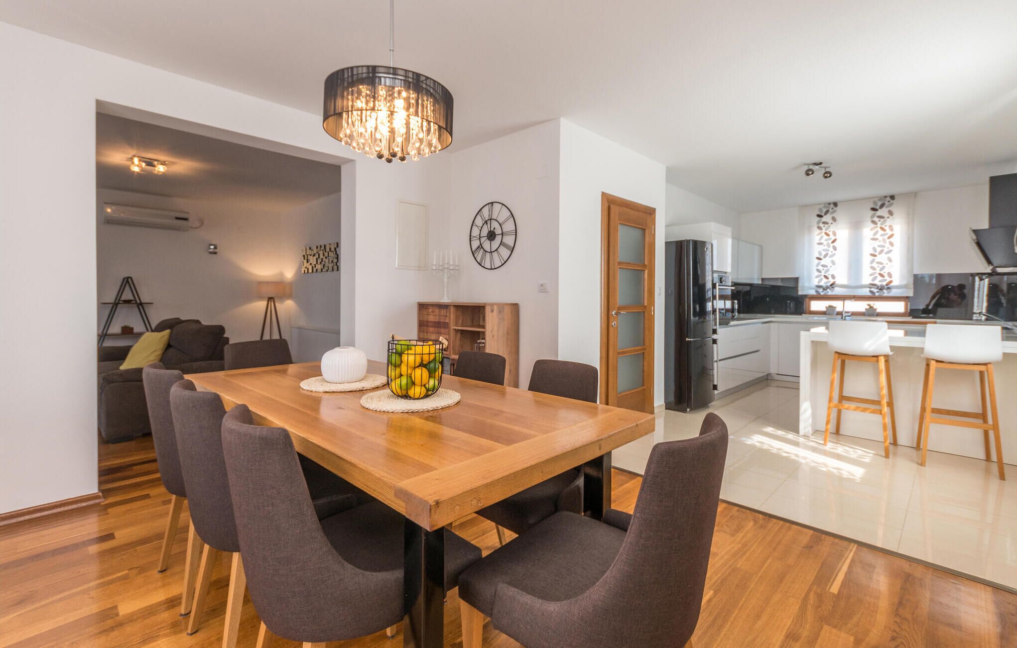 Een moderne keuken met witte kasten, een zwarte koelkast en een houten eettafel met vier stoelen.